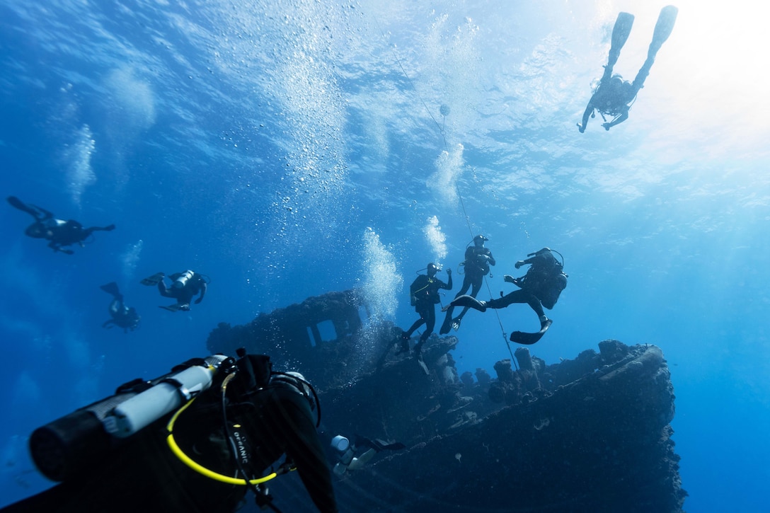 U.S., Mexican, Australian and Canadian naval divers swim in a body of water near a sunken ship.