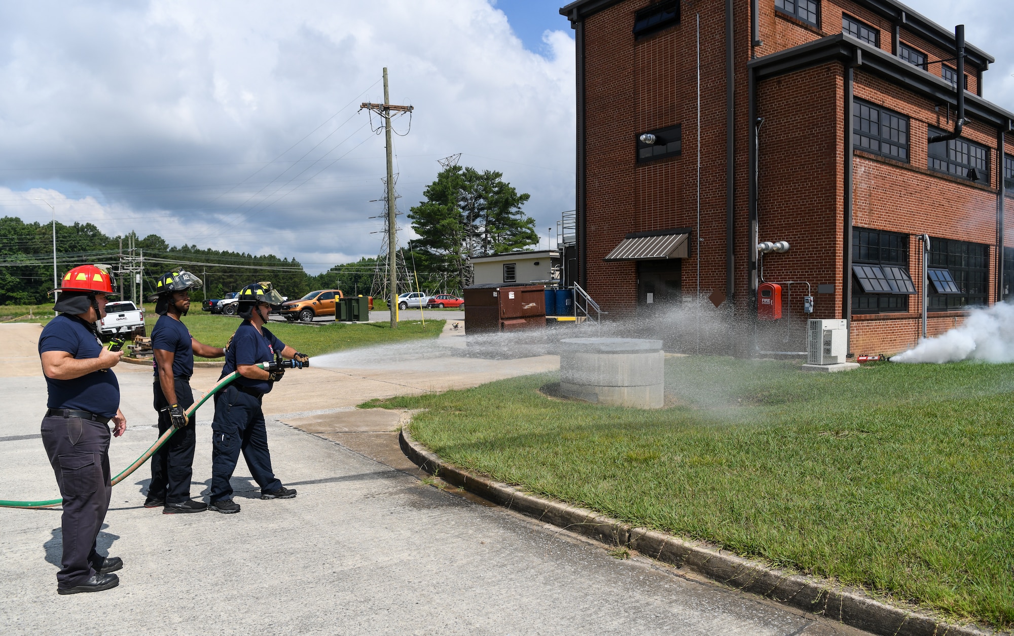 Two firefighters using a fire hose and one standing by with radio