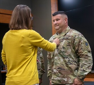 Amanda Nokes, spouse of newly promoted Illinois Army National Guard Col. Shawn Nokes, of Springfield, Illinois, secures his new rank during a promotion ceremony Aug. 1 at the Illinois Military Academy, Camp Lincoln in Springfield, Illinois.