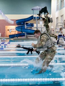 A soldier wearing combat equipment jumps into a pool