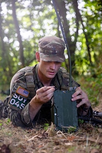A soldier lays in the prone position and programs a radio.