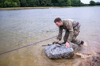 A soldier moves a moves his equipment bundled in a tard through a water obstacle.