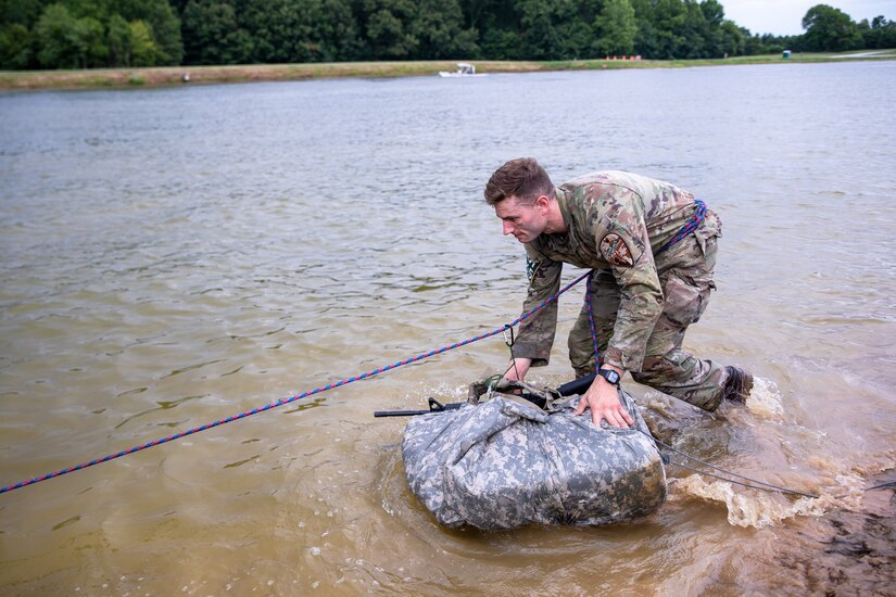 A soldier moves a moves his equipment bundled in a tard through a water obstacle.