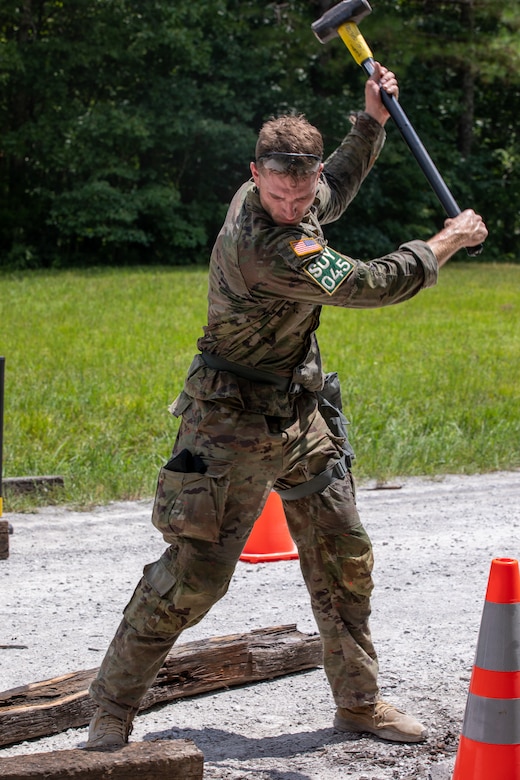 A soldier uses a sledgehammer to to drive a railroad tie.