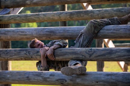 A soldier climbs through log obstacles on an obstacle course.