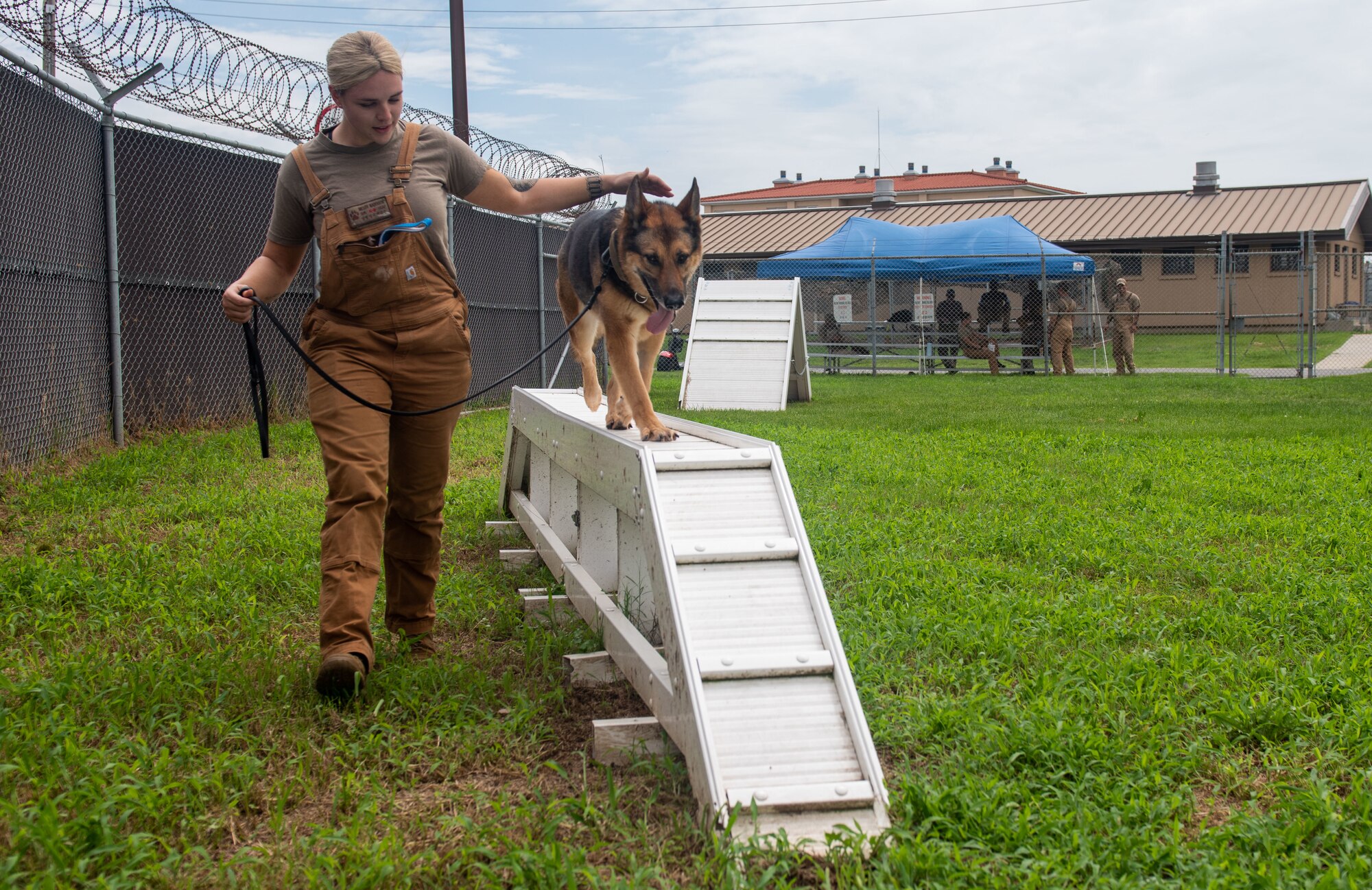 A military member walks her working dog over an obstacle course.