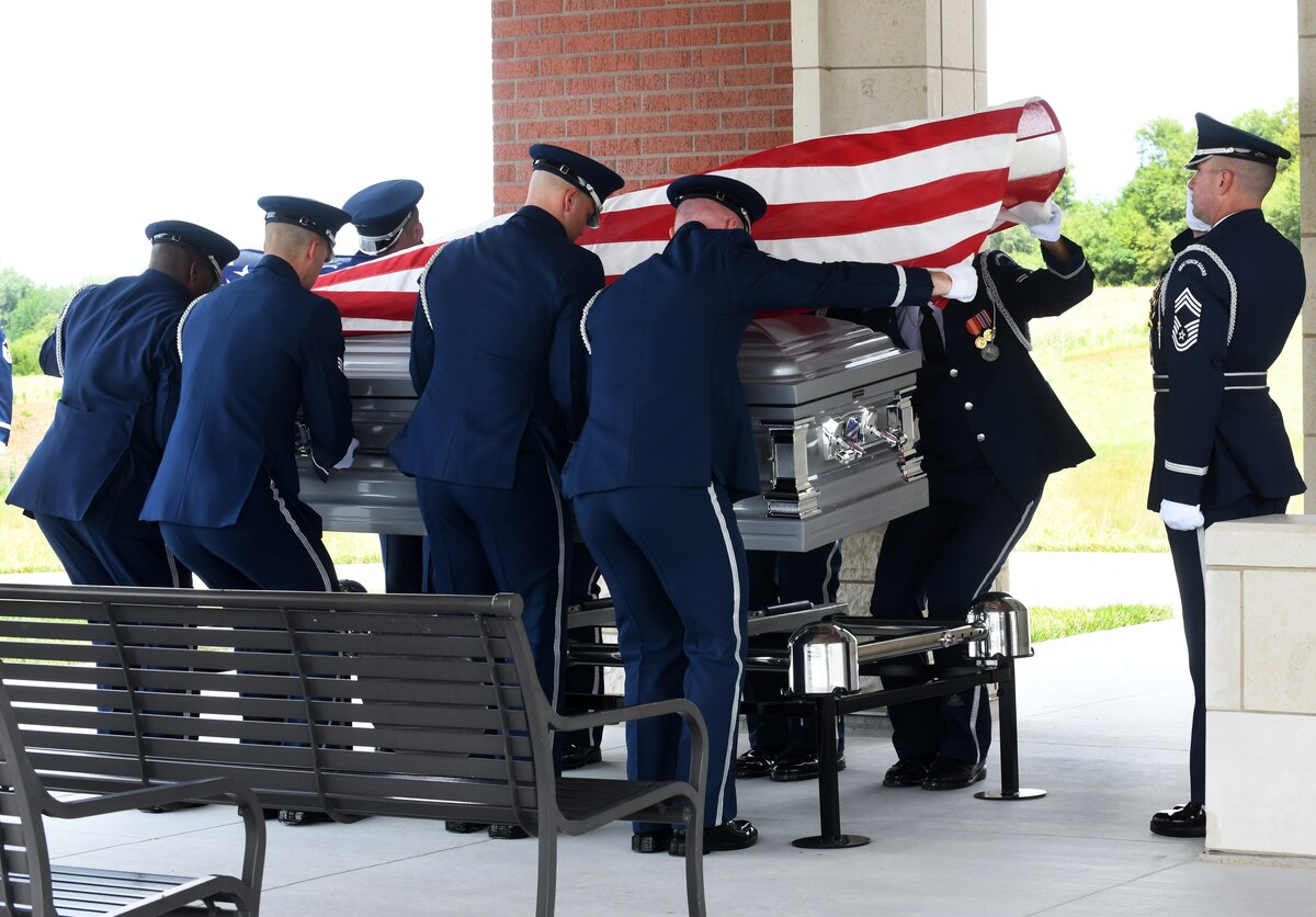 Uniformed Airmen lower a U.S. flag-covered casket onto a stand.