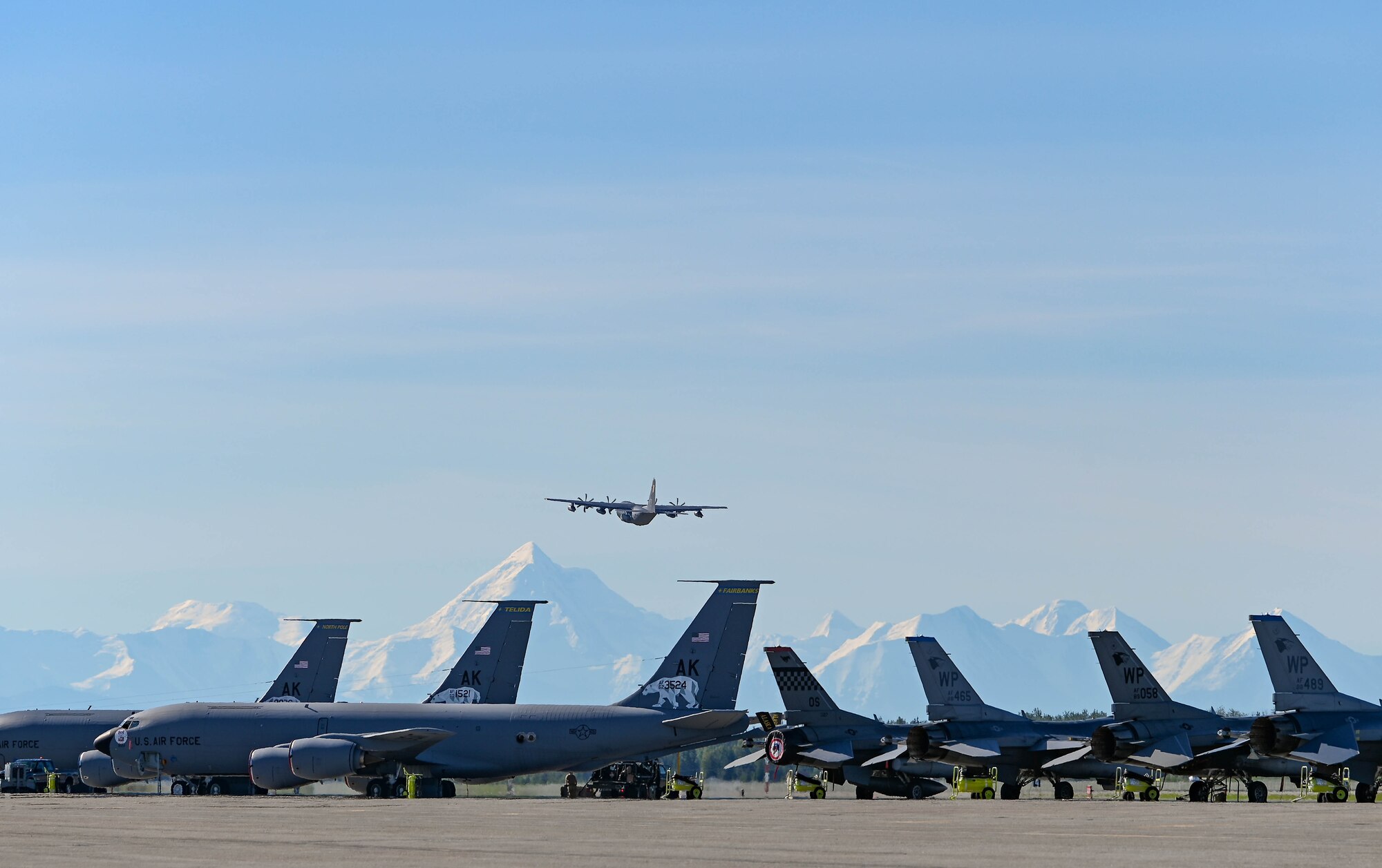 A military aircraft takes off above a row of other military aircraft.