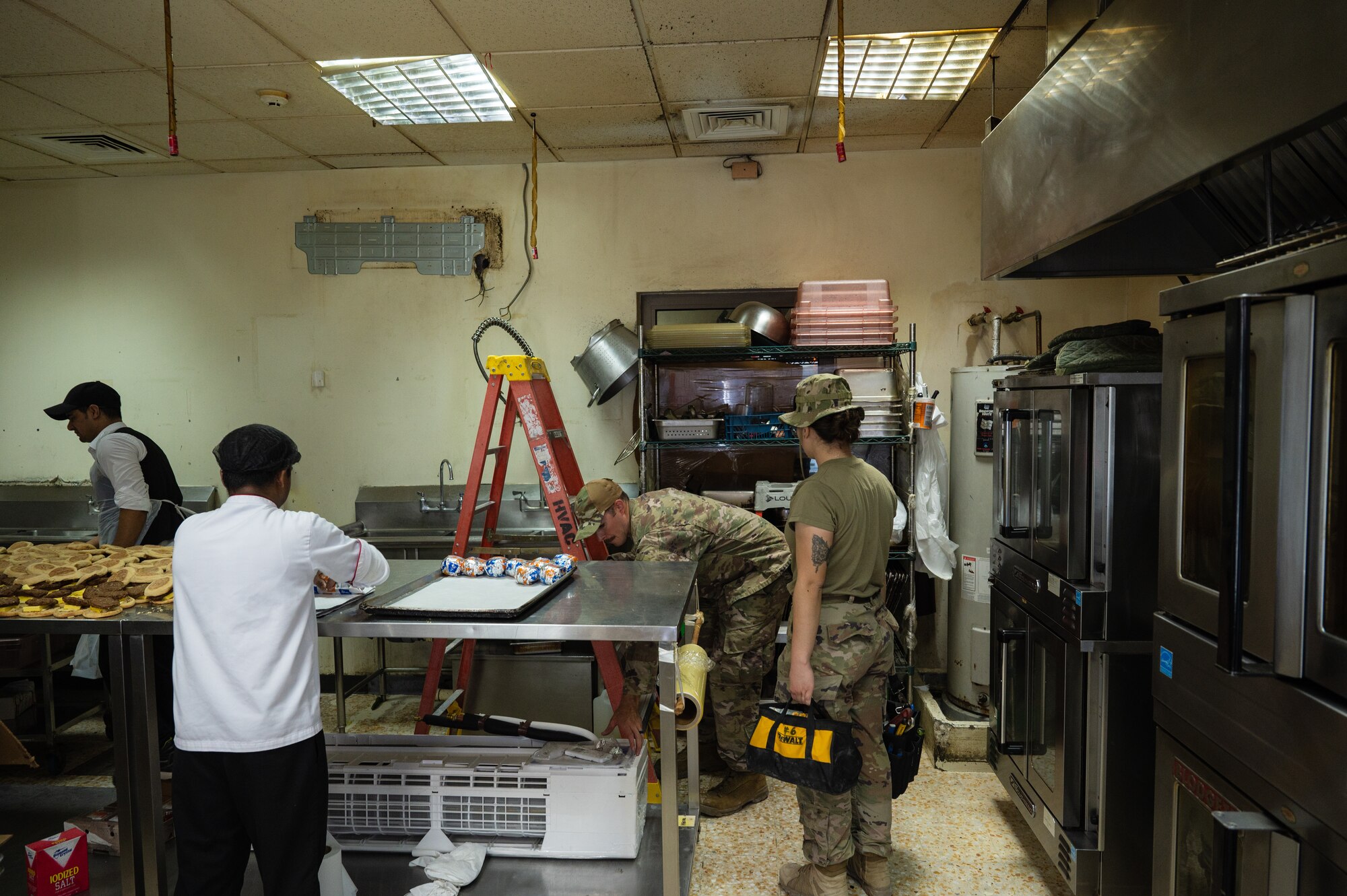 U.S. Air Force Staff Sgt. Jonathan Duffner (center) and Airman 1st Class Haunanionapua Wright (right), heating ventilation and air conditioning airmen from the 379th Expeditionary Civil Engineer Squadron, prepare to hang a mini-split air conditioner in the Hot Grab, July 29, 2022 at Al Udeid Air Base, Qatar. Mini-splits have provided air conditioning to buildings all over the base which were not designed with ductwork. (U.S. Air Force photo by Staff Sgt. Dana Tourtellotte)