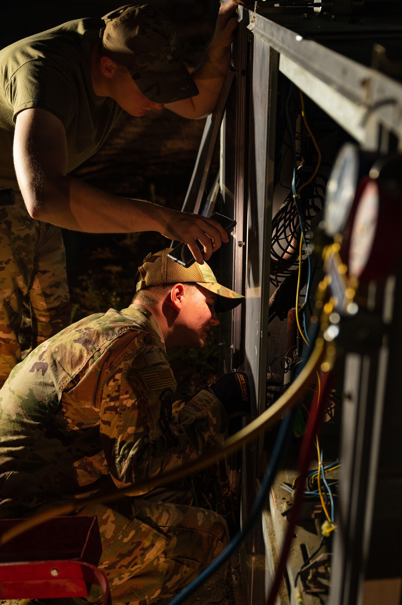 U.S. Air Force Staff Sgt. Robert Milliner (center) and Airman 1st Class Kyle Kersey (top left), heating ventilation and air conditioning airmen from the 379th Expeditionary Civil Engineer Squadron, explore the inner workings of a cooling unit looking for a pipe leak, July 29, 2022 at Al Udeid Air Base, Qatar. The Airmen used special gas and gauges to help them determine that a leak was the problem with the unit. (U.S. Air Force photo by Staff Sgt. Dana Tourtellotte)