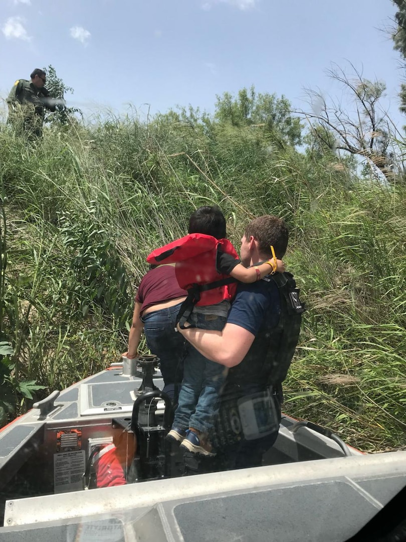 Members from Coast Guard Maritime Safety & Security Team Houston transfer a child and woman to U.S. Border Patrol agents waiting on the U.S. riverbank of the Rio Grande, June 16, 2022. The people tried to cross the river aboard an overcrowded raft alongside 10 other non-citizens. (U.S. Coast Guard photo, courtesy Maritime Safety & Security Team Houston)