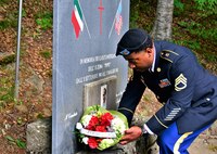 The Army Field Support Battalion-Africa intelligence and operations noncommissioned officer in charge, Sgt. 1st Class Tehran Jones, lays flowers at the base of the memorial site for Manrico Ducceschi, also known as Pippo, during a Italian-American commemorative ceremony in Pianaccina Pian di Novello, July 31. “I will continue to support this ceremony as long as I'm stationed here,” said Jones. (Photo by Elena Baladelli)