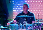 Ken Reiner plays a drum set on a stage.