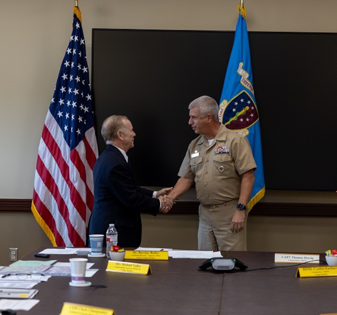 Dr. Barclay Butler, Assistant Director for Support, Defense Health Agency, congratulates Navy Capt. Thomas Herzig, outgoing Commandant of the Medical Education and Training Campus (METC) during a low-key Change of Commandant ceremony held July 21 at the Medical Education and Training Campus (METC) on Joint Base San Antonio-Fort Sam Houston, Texas. Air Force Col. David Walmsley became the sixth METC commandant.