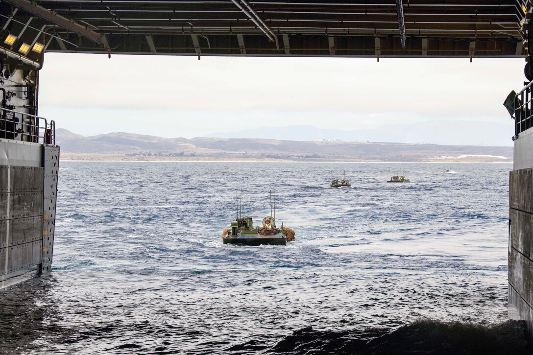 Marines in small boats approach a ship in a body of water.