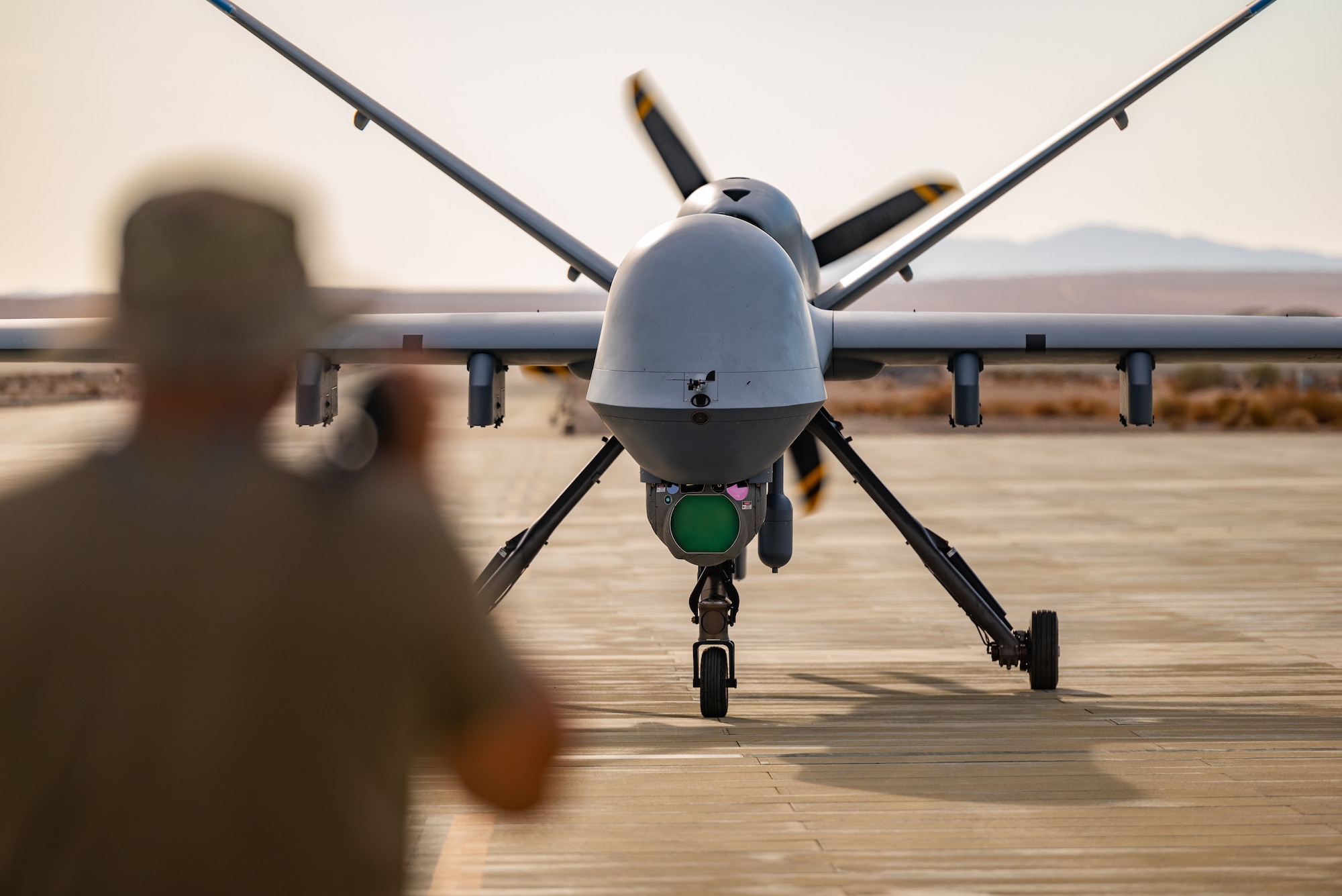 A Crew Chief assigned to the 163d Attack Wing, March Air Reserve Base marshals MQ-9 Reaper on the Strategic Expeditionary Landing Field on Marine Corps Air Ground Combat Center Twentynine Palms, California, July 21, 2022. The 163d accelerated change by pioneering the first ever refueling of the MQ-9 Reaper using a Forward Area refueling Point provided by the VMM - 764’s V-22 Osprey. (U.S. Air National Guard photo by Staff Sgt. Joseph Pagan)