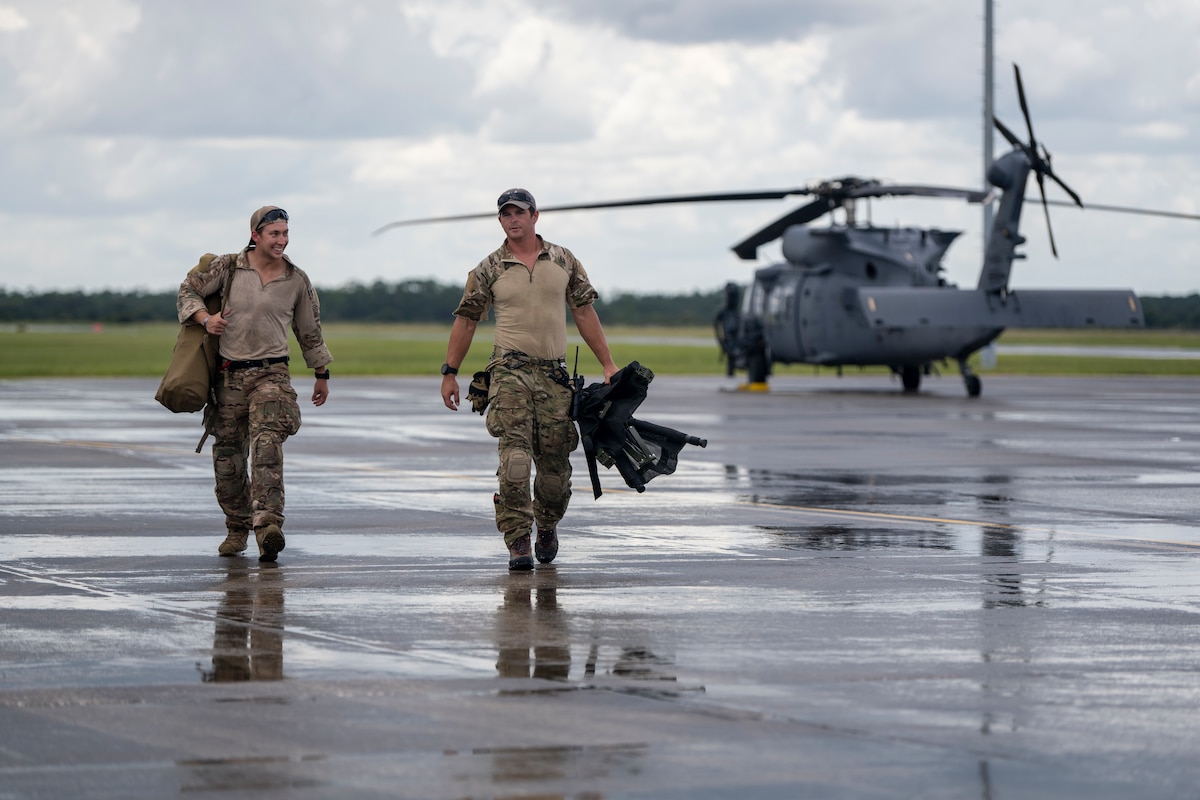 Two pararescuemen walk away from an HH-60W Jolly Green II helicopter after a rainstorm.