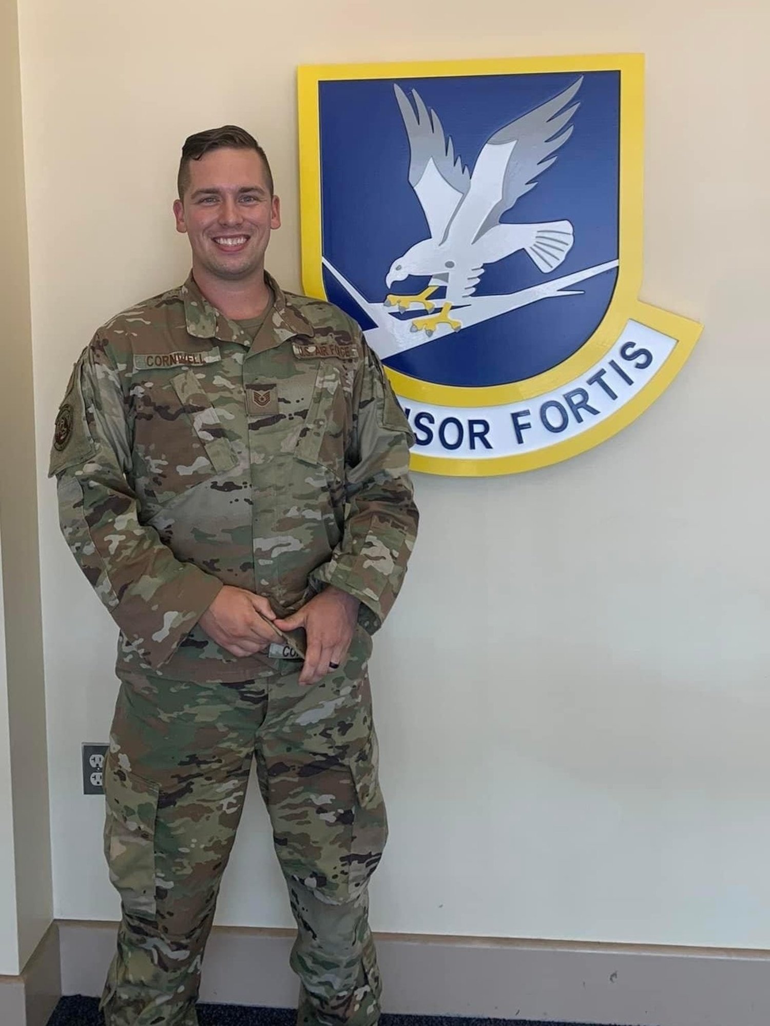 Tech. Sgt. Jonah Cornwell, 66th Security Forces Squadron defender, poses in front of a Defensor Fortis emblem affixed to a wall at Hanscom Air Force Base, Mass. Last month, Cornwell was notified by his leadership team that he had been accepted into the Officer Training School at Maxwell AFB, Ala. (U.S. Air Force courtesy photo)