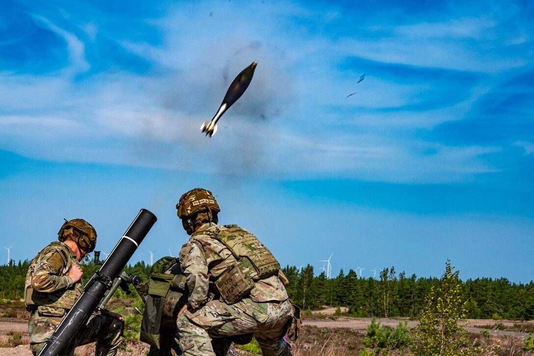 Two soldiers watch as a mortar round soars into the air.