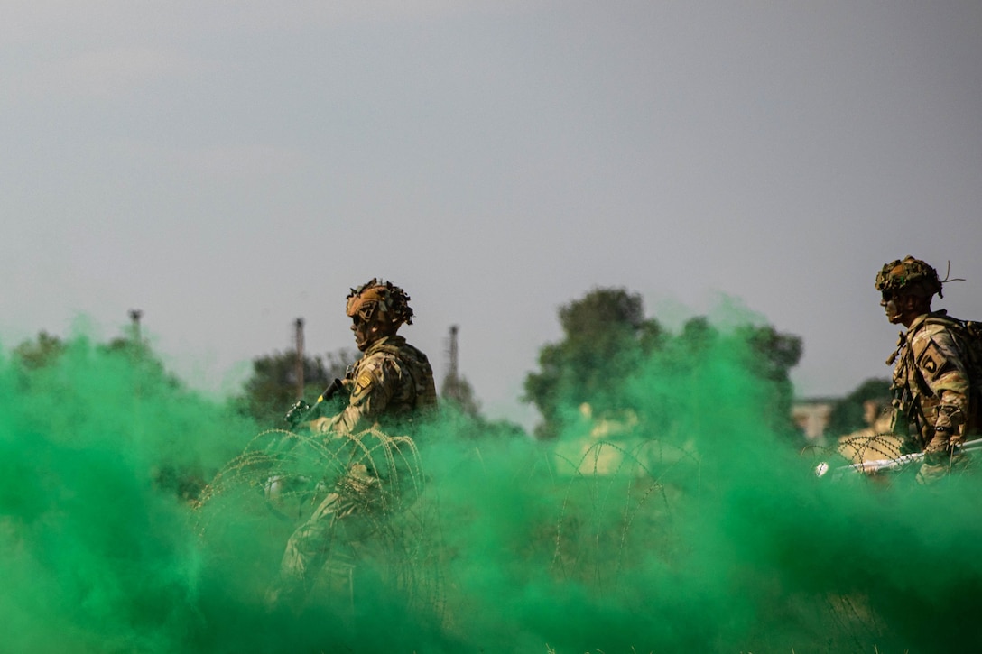 Two soldiers walk through green smoke.