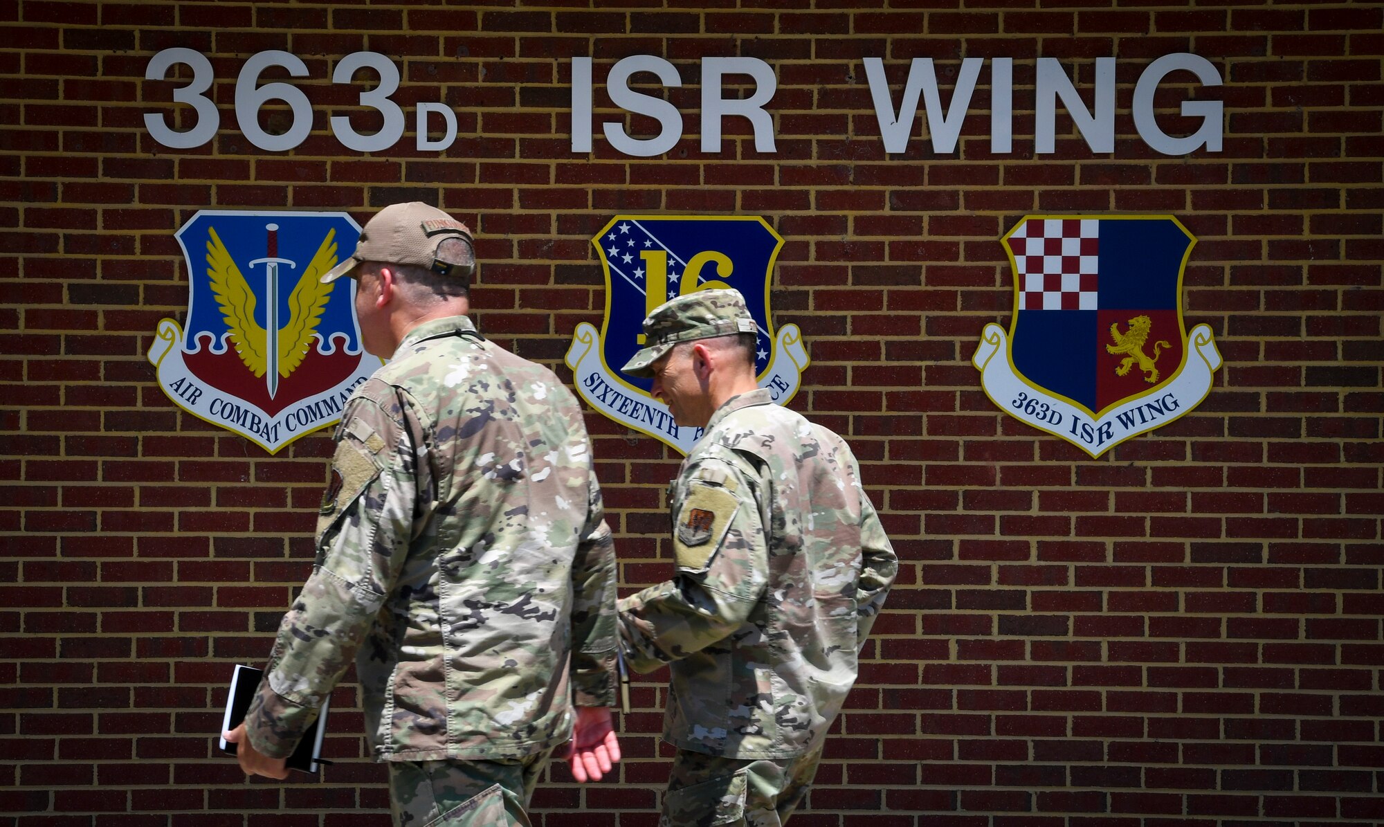 Two individuals walk in front of the 363d ISR Wing emblem.