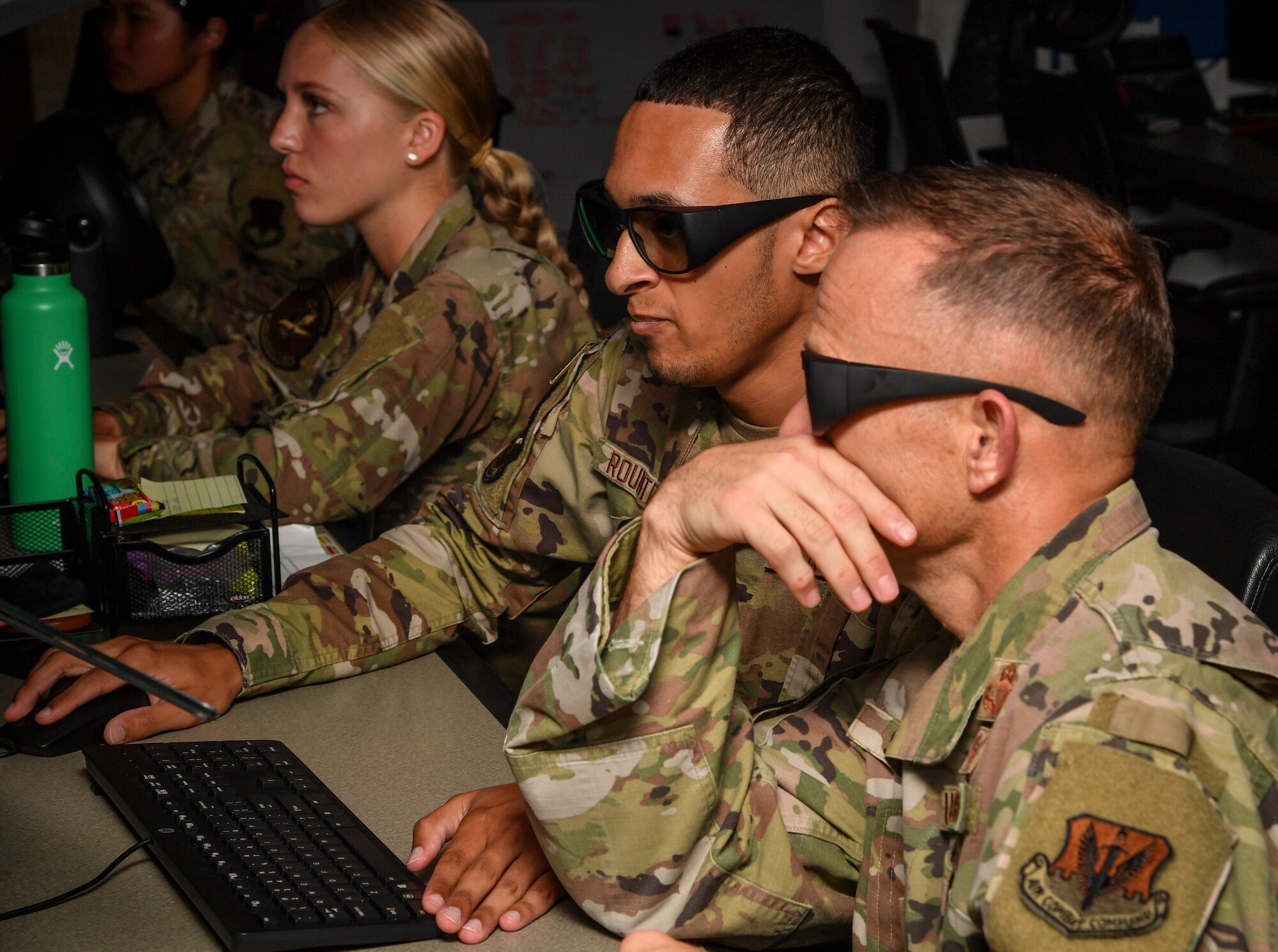 Two individuals sit in front of a monitor wearing special glasses.