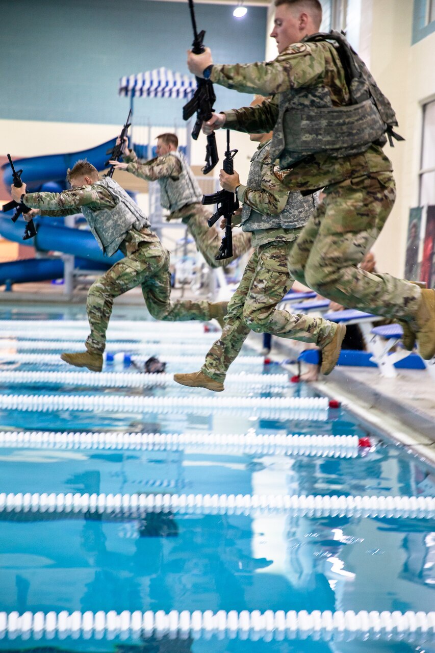 Soldiers in camouflage uniforms holding rifles jump into a pool.