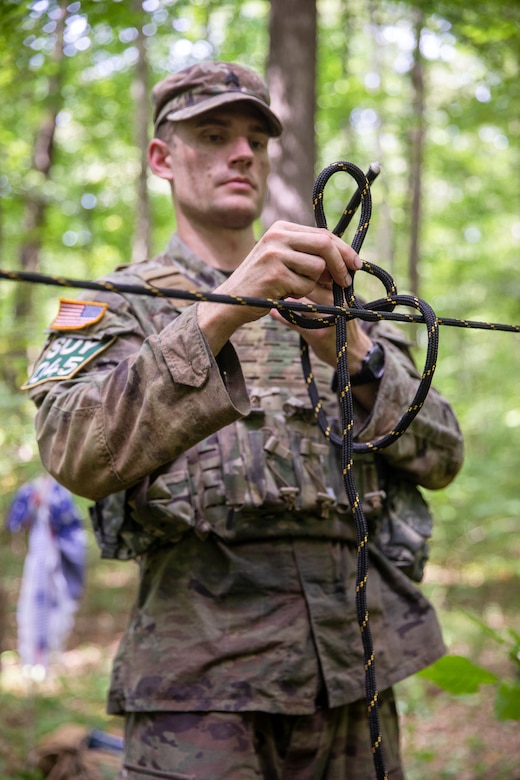 A soldier ties black cord into a knot outdoors.