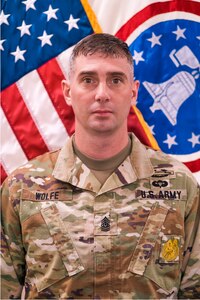 Soldier in uniform in front of flag.