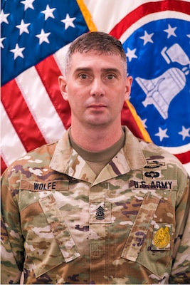 Soldier in uniform in front of flag.