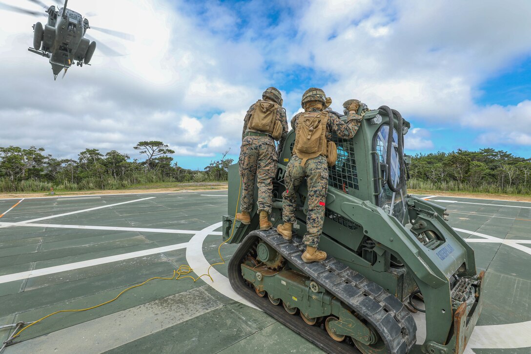 A group of Marines stand together as a helicopter flies overhead.