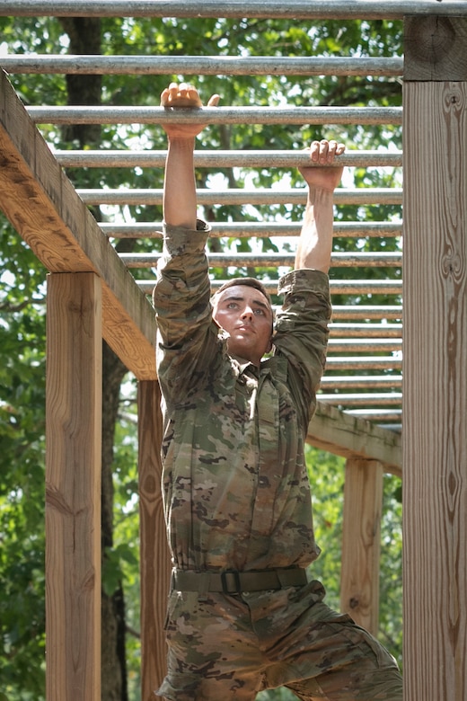 A soldier hangs from monkey bars outside.