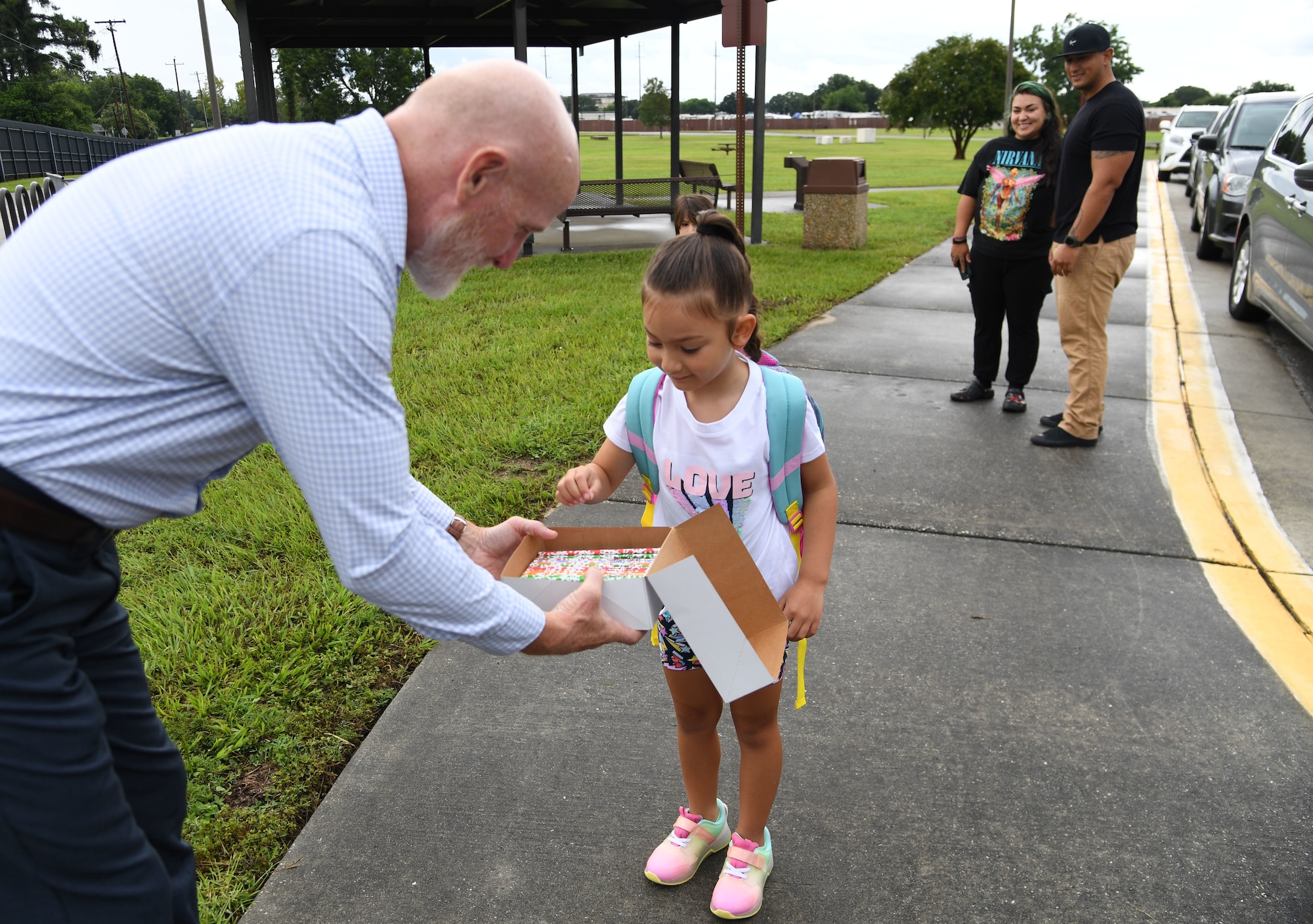 Gerald Cross, 81st Force Support Squadron school liaison officer, offers pencils to Carina Patruno for the first day of school as her parents, U.S. Army Sgt. 1st Class Jason Patruno, 177th Armor Brigade observer coach trainer, at Camp Shelby, Mississippi, and Alyssa, stand by near the pedestrian gate at Keesler Air Force Base, Mississippi, Aug. 4, 2022. Members of the 81st Security Forces Squadron and Chase the Paw Patrol dog also welcomed military children as they went to Back Bay Elementary School. (U.S. Air Force photo by Kemberly Groue)
