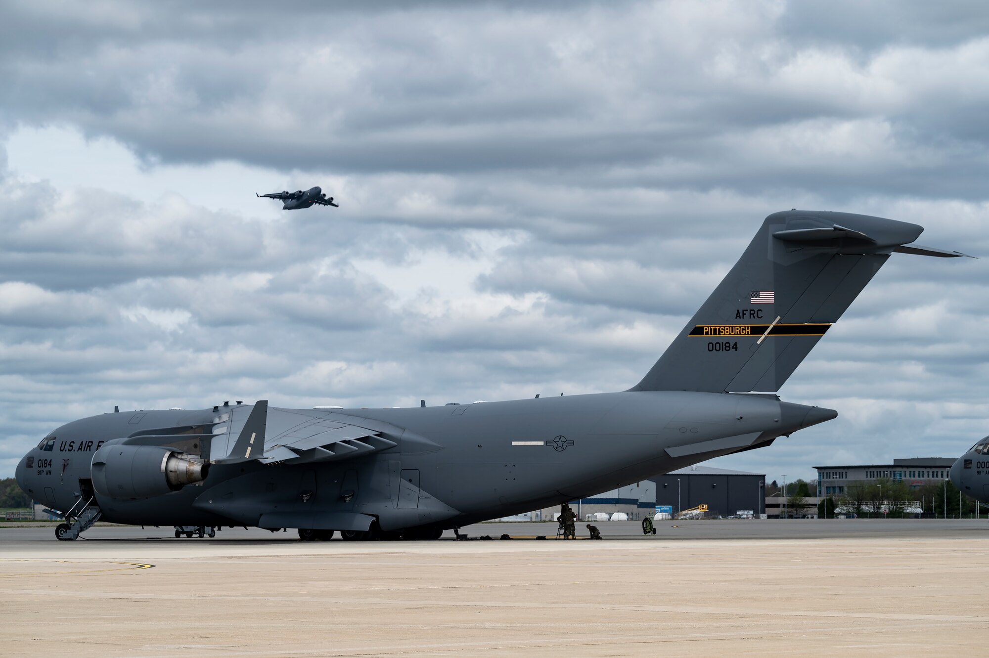 Airmen assigned to the 911th Aircraft Maintenance Squadron conduct routine maintenance on a C-17 Globemaster III as another C-17 assigned to the 911th Airlift Wing flies a training mission over the Pittsburgh International Airport Air Reserve Station, Pennsylvania, May 5, 2022.