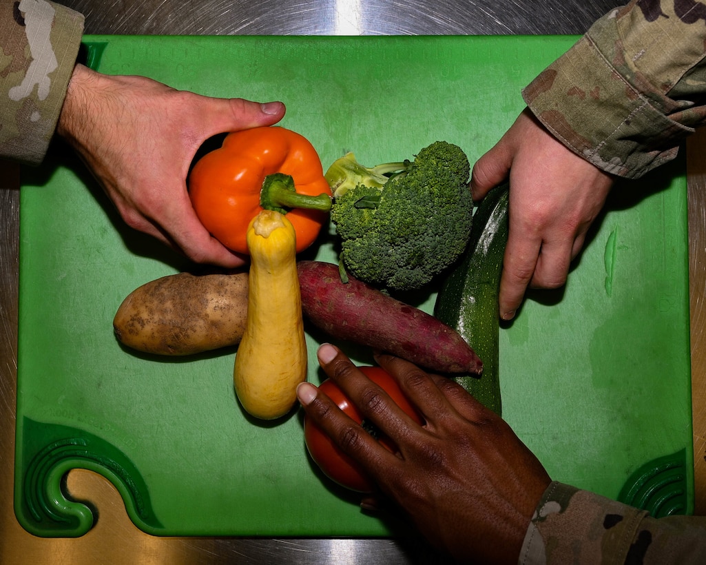 Hands in military uniforms reach for different vegetables.