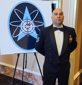 U.S. Air Force Tech Sgt. Ryan Colon, a 114th Space Control Squadron weapons instructor, in front of a graphic of the enlisted weapons patch following his graduation from the Space Warfighter Advanced Instructor Course at Nellis Air Force Base, Nevada, in June 2022. Colon is the first enlisted Airman in the Air National Guard to graduate from the Space Warfighter Advanced Instructor Course.