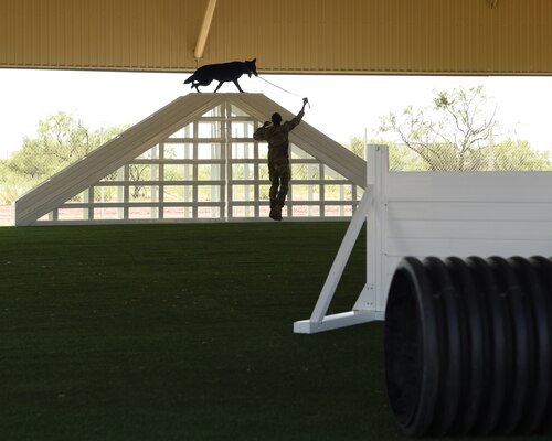 U.S. Air Force Staff Sgt. Damon Hunt, 17th Security Forces Squadron military working dog handler, guides MWD Aghi, through a training obstacle course at Goodfellow Air Force Base, Texas, Aug. 3, 2022. The covered outdoor military working dog structure was an infrastructure upgrade made possible by a $5.2 million Defense Economic Adjustment Assistance Grant. (U.S. Air Force photo by Senior Airman Abbey Rieves)