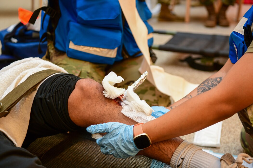 Airmen from the 5th Medical Group wraps a compression bandage around a simulated leg injury during exercise Ready Eagle in the 5th MDG building on Minot Air Force Base Aug. 3, 2022. The exercise allowed Airmen to train and practice Tactical Combat Casualty Care (TCCC), the decontamination process (DCON), and operating in high-tempo situations to prepare them for possible future incidents. (U.S. Air Force photo by Airmen Alysa Knott)