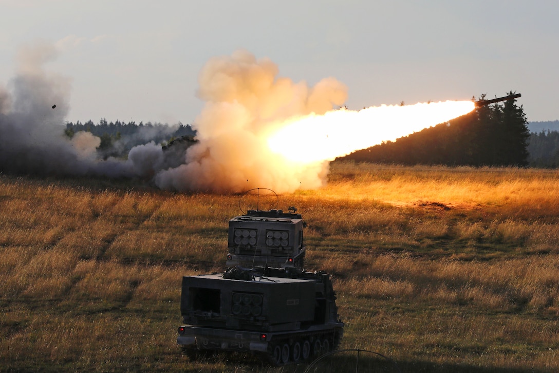 A missile streaks across the sky leaving smoke and fire in its wake; two rocket-equipped armored vehicles are in the foreground.