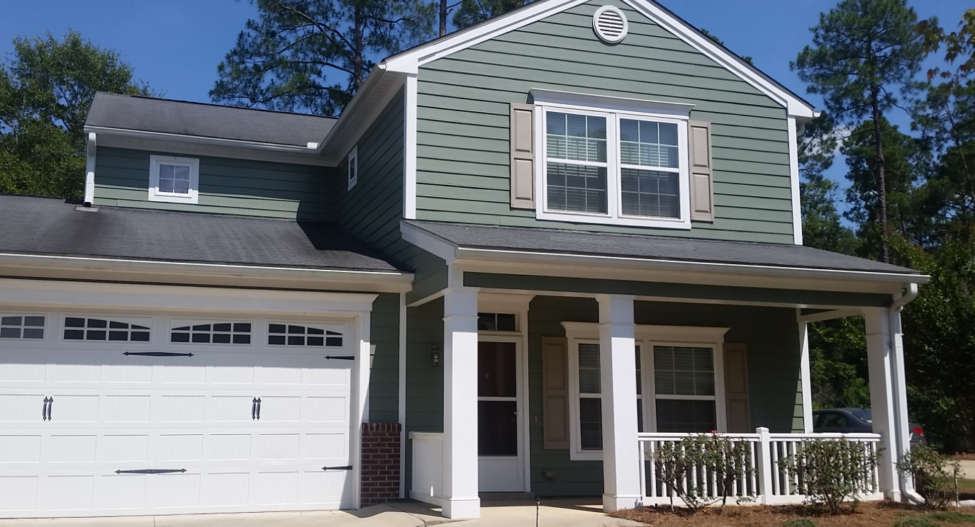 Front of a green house with a garage attached on the left.