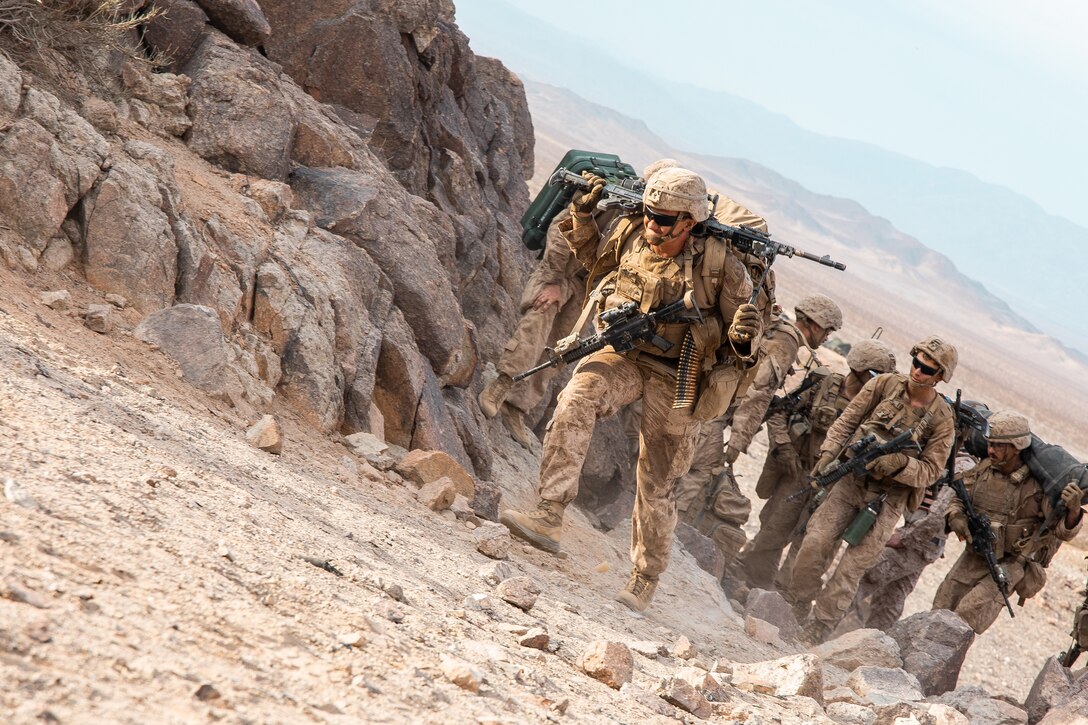 A group of Marines walk up a hill in the desert.