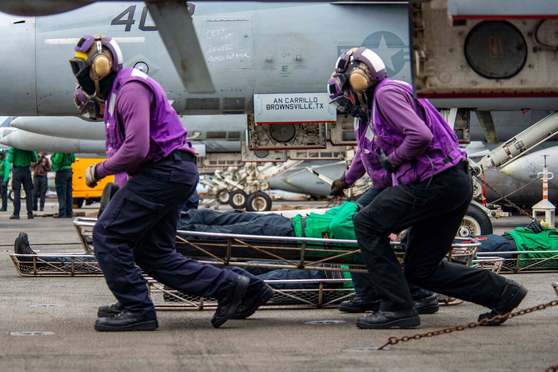 Sailors carry another sailor on a stretcher.