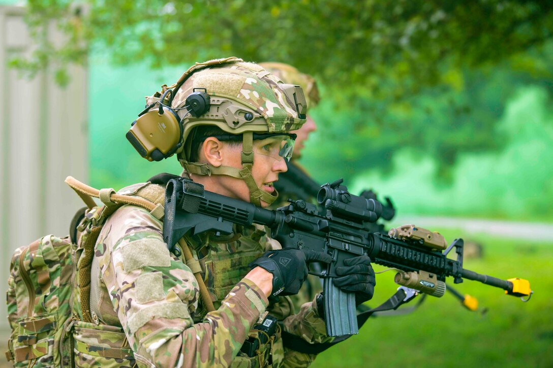 An airman walks through a wooded area while holding a weapon.