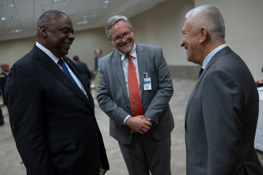 Three men in formal business attire smile as they stand and talk.