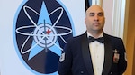 U.S. Air Force Tech Sgt. Ryan Colon, a 114th Space Control Squadron weapons instructor, in front of a graphic of the enlisted weapons patch following his graduation from the Space Warfighter Advanced Instructor Course at Nellis Air Force Base, Nevada, in June 2022.