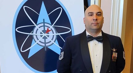 U.S. Air Force Tech Sgt. Ryan Colon, a 114th Space Control Squadron weapons instructor, in front of a graphic of the enlisted weapons patch following his graduation from the Space Warfighter Advanced Instructor Course at Nellis Air Force Base, Nevada, in June 2022.