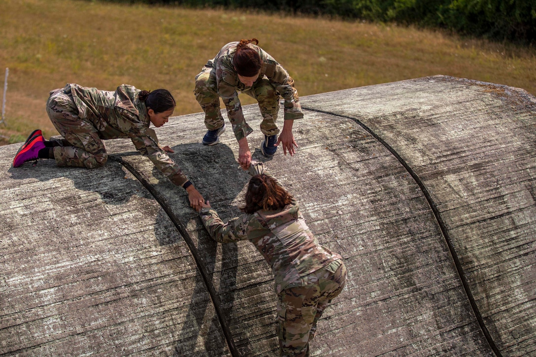 Two soldiers help a fellow soldier climb an obstacle.