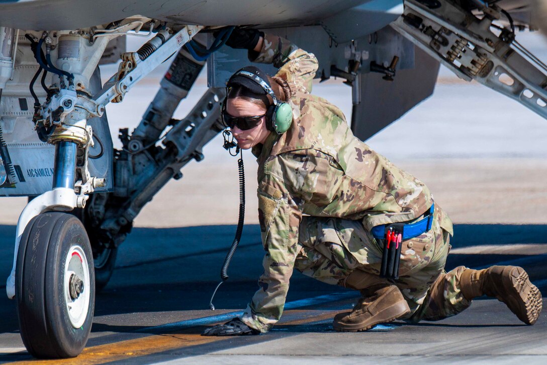 An airman kneels underneath an aircraft.