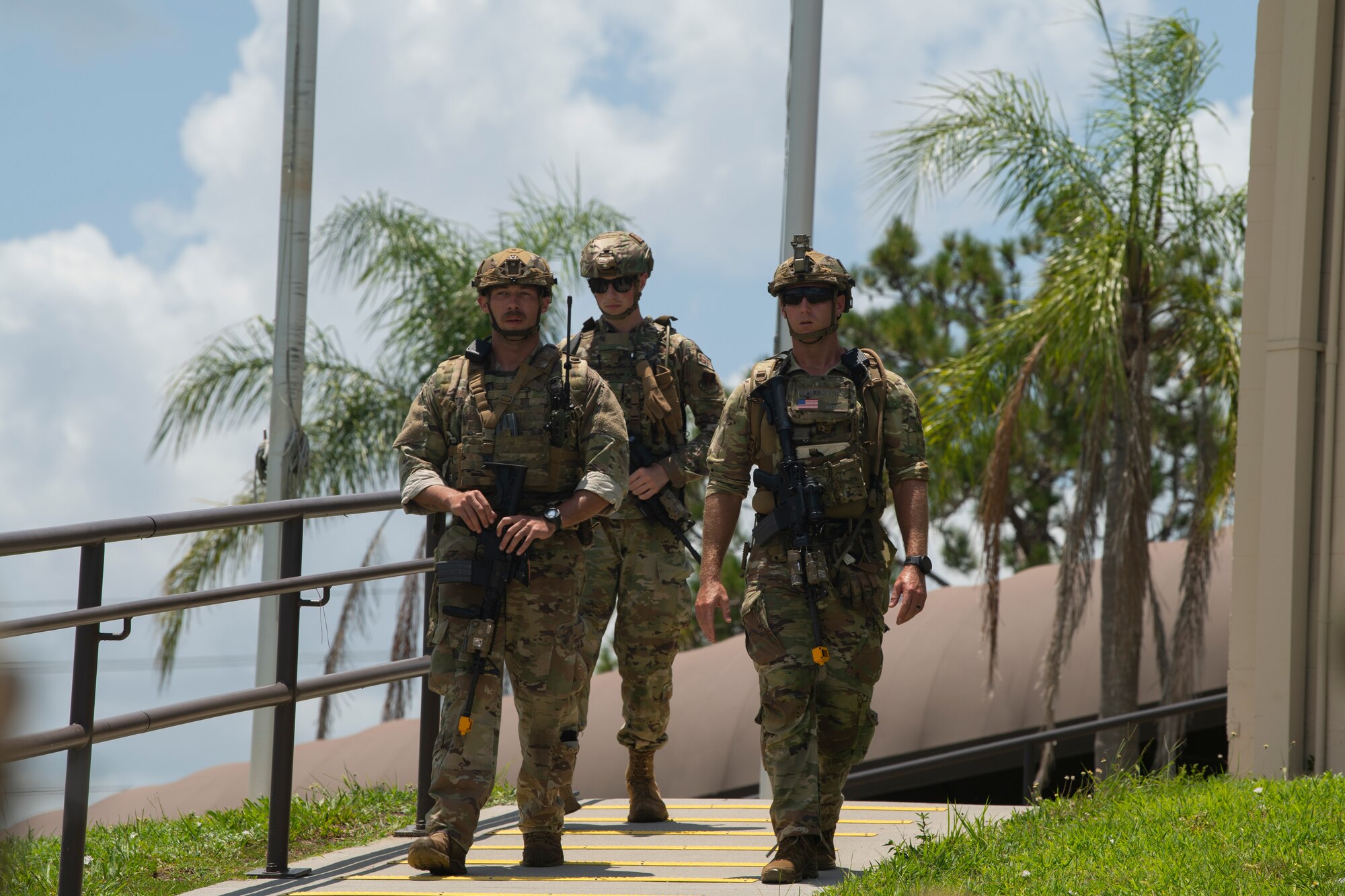 A photo of three Airmen walking down a slanted hill with palm trees in the background.