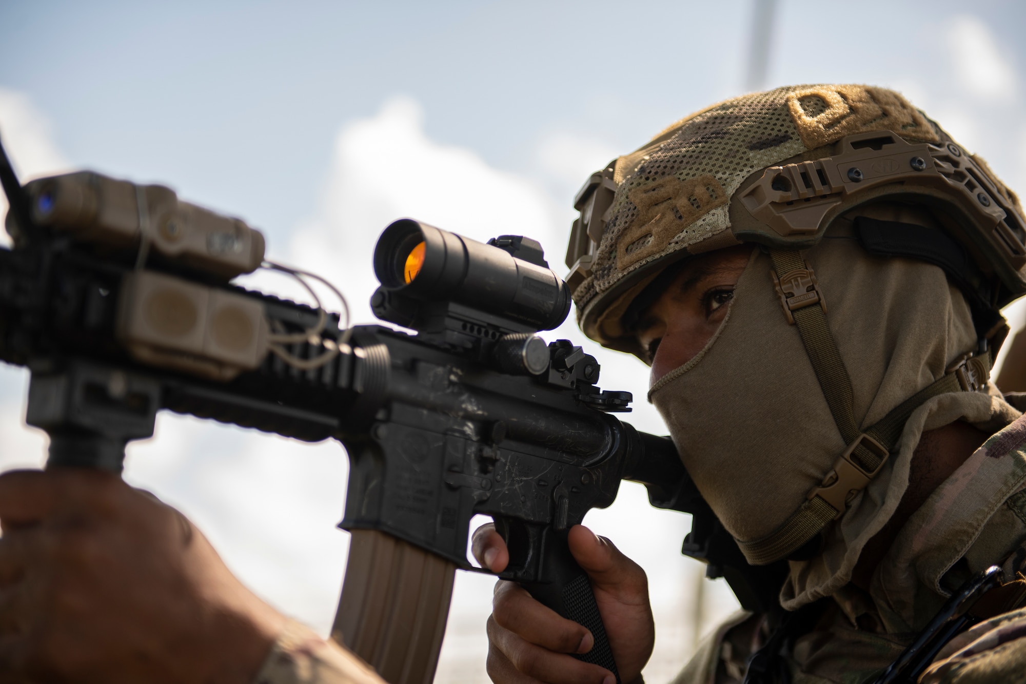 An up-close photo of an Airman holding an M-4 Carbine scope up to his eye.